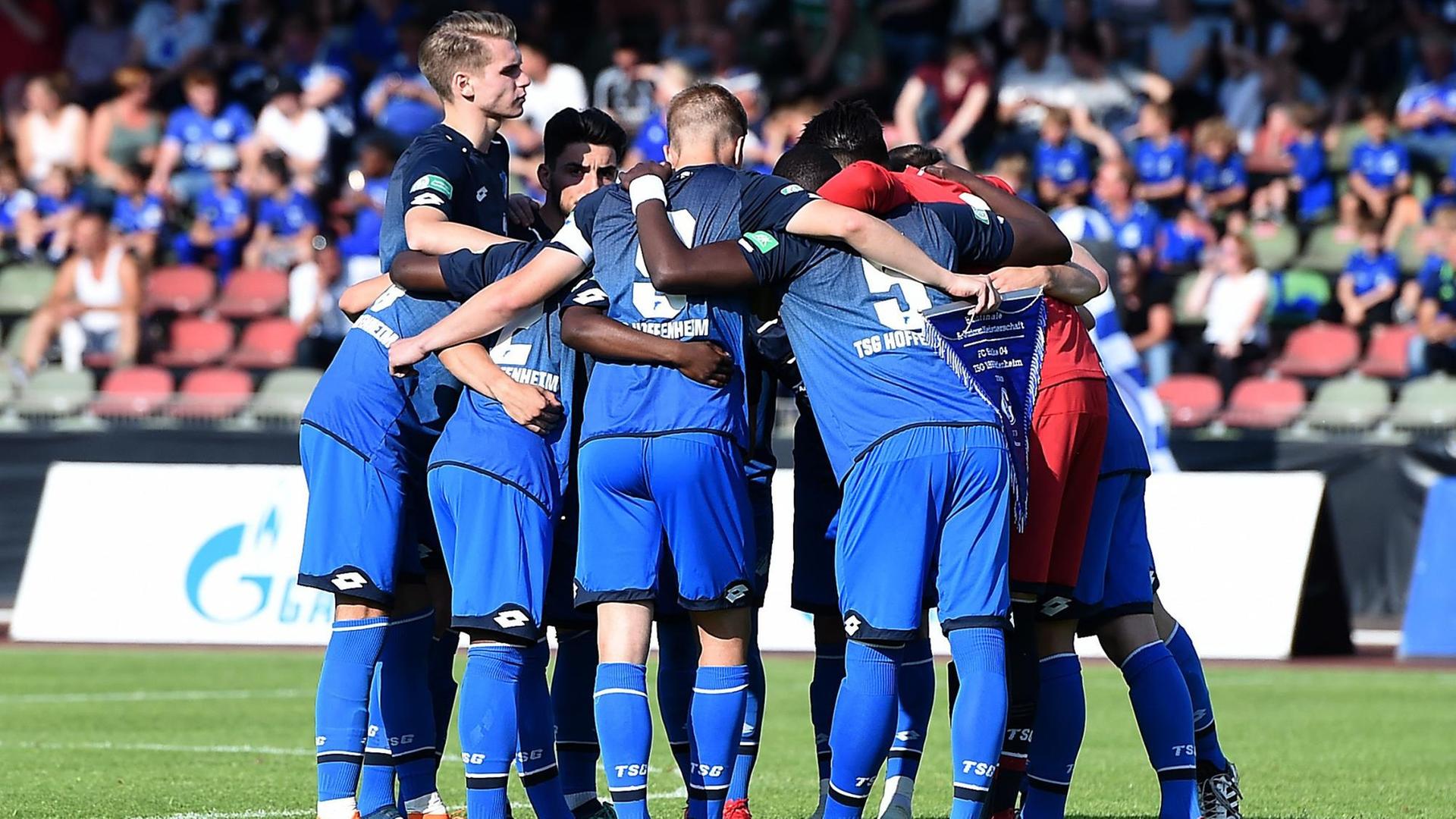 Das Bild zeigt den Kreis der blaugekleideten Hoffenheimer auf dem Rasen, im Hintergrund unscharf eine nicht ganz vollbesetzte Tribüne. Das Bild zeigt den Kreis der blaugekleideten Hoffenheimer auf dem Rasen, im Hintergrund unscharf eine nicht ganz vollbesetzte Tribüne.