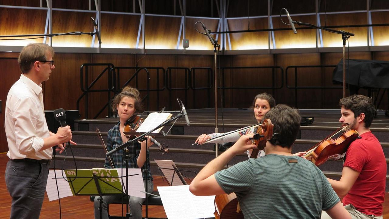 Die Musiker des Aris Quartett sitzen mit ihren Streichinstrumenten in der Hand im Halbkreis zwischen Mikrofonen im Deutschlandfunk Kammermusiksaal und werden von Moderator Christoph Schmitz interviewt.