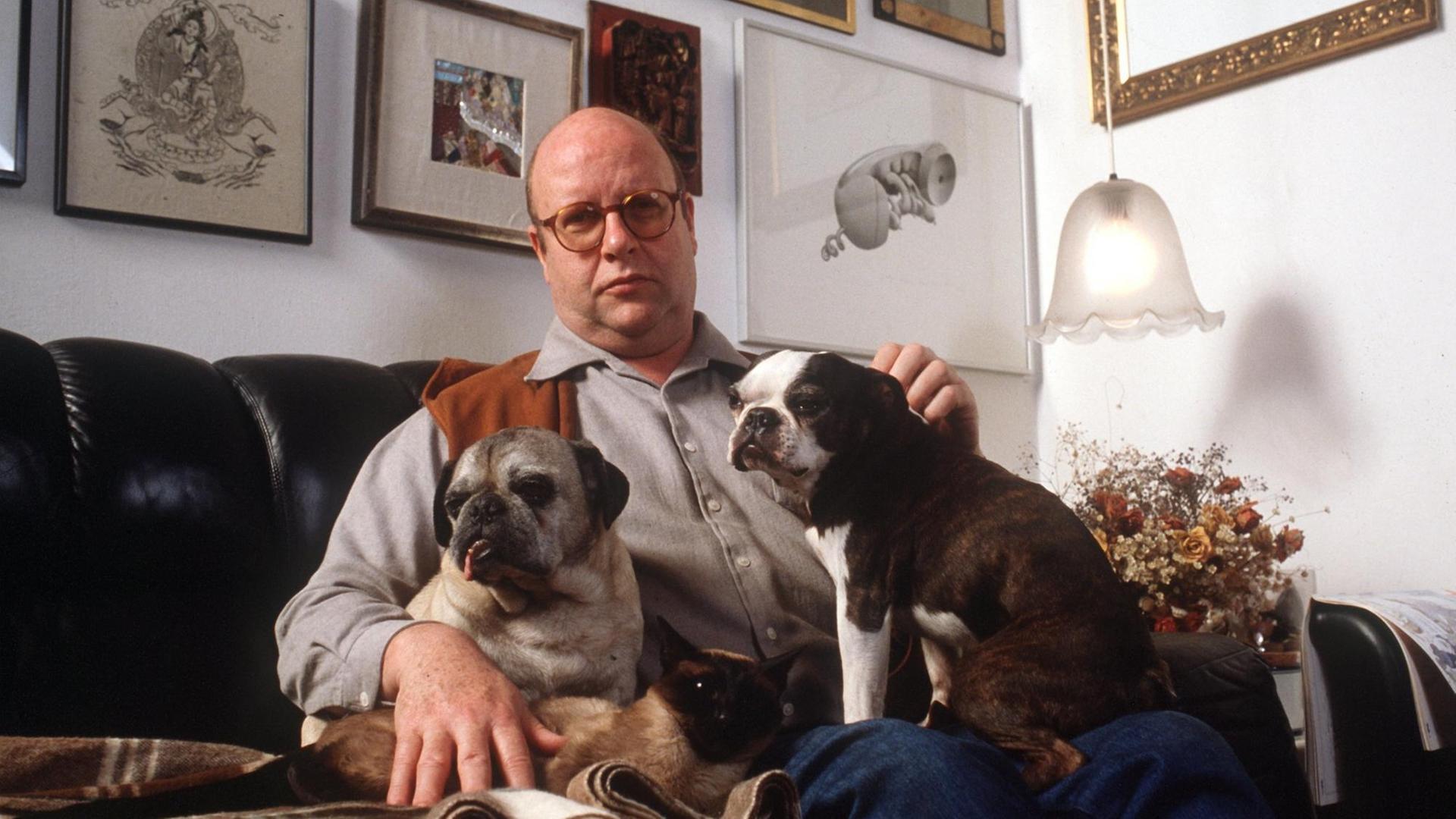 Der deutsche Schauspieler Gert Haucke sitzt auf dem Sofa im Wohnzimmer seines Hauses in der Lüneburger Heide mit seinen beiden Möpsen Kasper und Bobo (l) und der Siamkatze Koschka. Aufnahme von 1983.