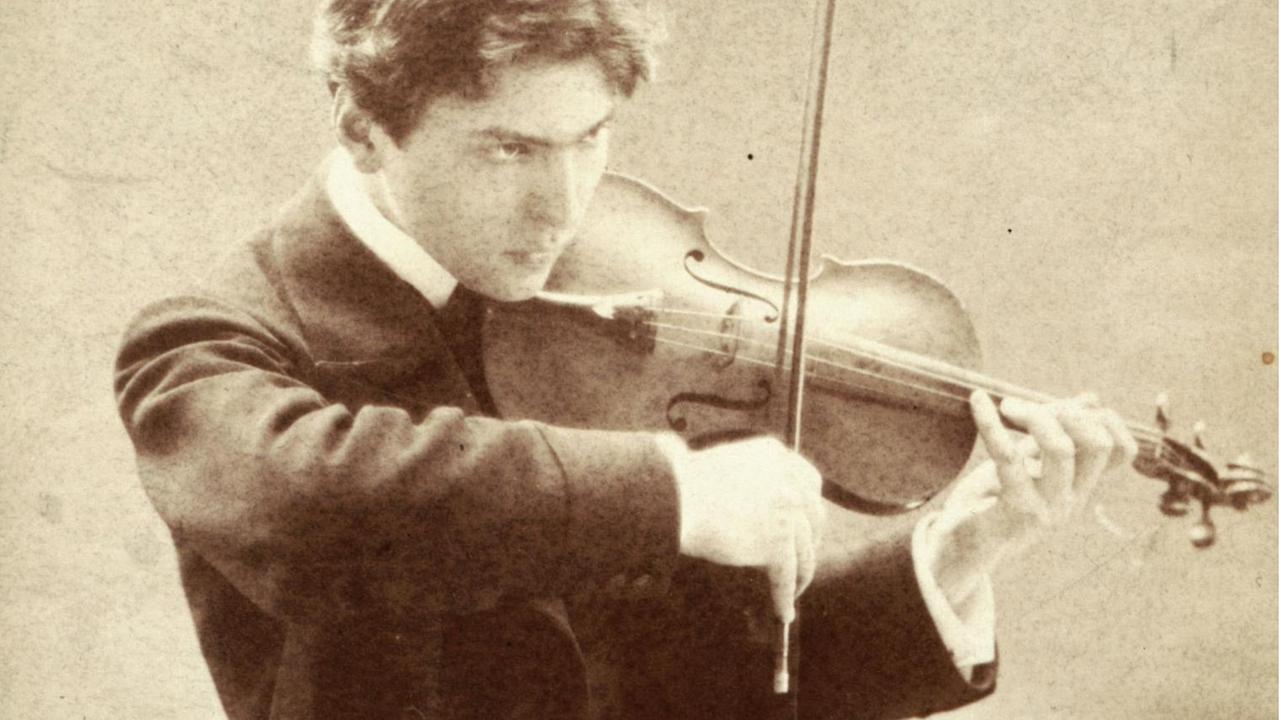 Auf einer vergilbten Fotografie ist ein junger Mann in Abendkleidung beim Violinspiel zu sehen.