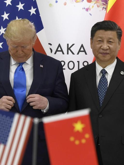 Donald Trump richtet seinen Anzug, während er auf dem G20-Gipfel mit Xi Jinping für ein Foto posiert.