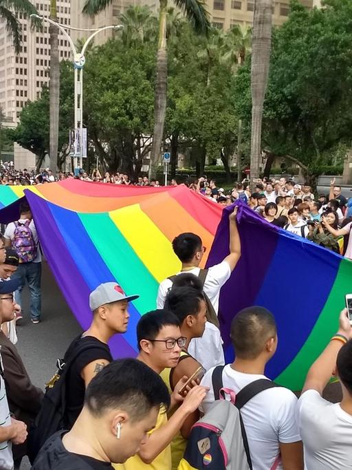 Vor allem männliche Teilnehmer der Gay Pride in Taipeh im Oktober 2017 tragen eine Regenbogenflagge durch die Straße.
