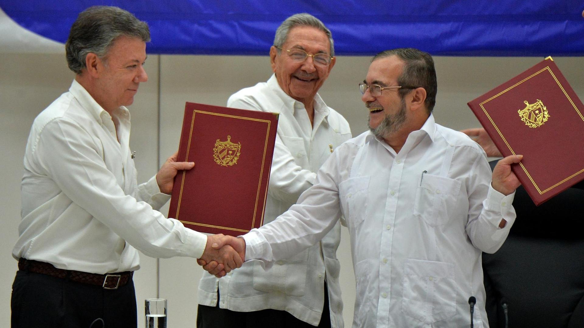 Kolumbiens Präsident Santos und FARC-Anführer Jimenez geben sich die Hand. Hinter ihnen steht der kubanische Präsident Castro, der in den Gesprächen vermittelt hatte.