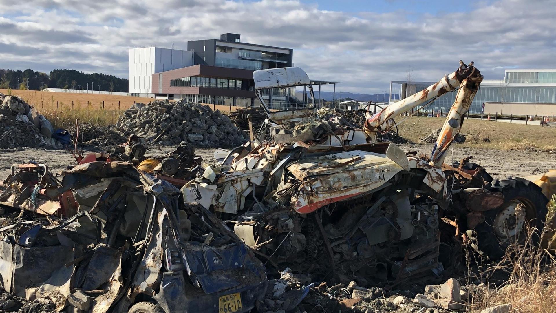Der gewaltige Tsunami überschwemmte vor zehn Jahren die ganze Küstenregion. Immer wieder sieht man noch Reste der Verwüstung, wie hier vorne im Bild den Schrott von Autos. Im Hintergrund dagegen das neue Fukushima: Das jüngst errichtete Museum über die nukleare Katastrophe.