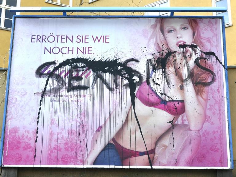 Über ein Plakat, dasss eine Frau in Dessous zeigt steht mit schwarzer Sprühfarbe "Sexismus" geschrieben.