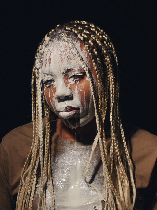 Das Bild zeigt die afroamerikanische Künstlerin Martine Syms, der weiße Flüssigkeit über das Gesicht läuft.
