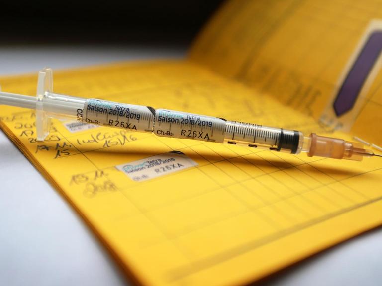 Eine Spritze liegt auf einem aufgeschlagenem Impfpass.