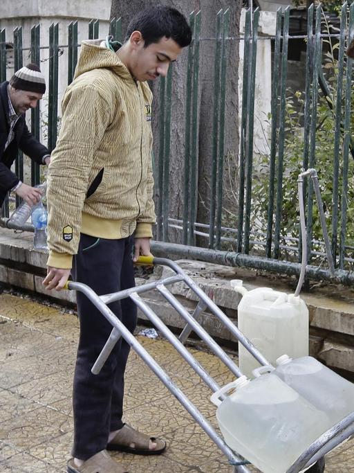Vier Syrer befüllen ihre Wasserkanister an einem öffentlichen Brunnen der Hauptstadt Damaskus.