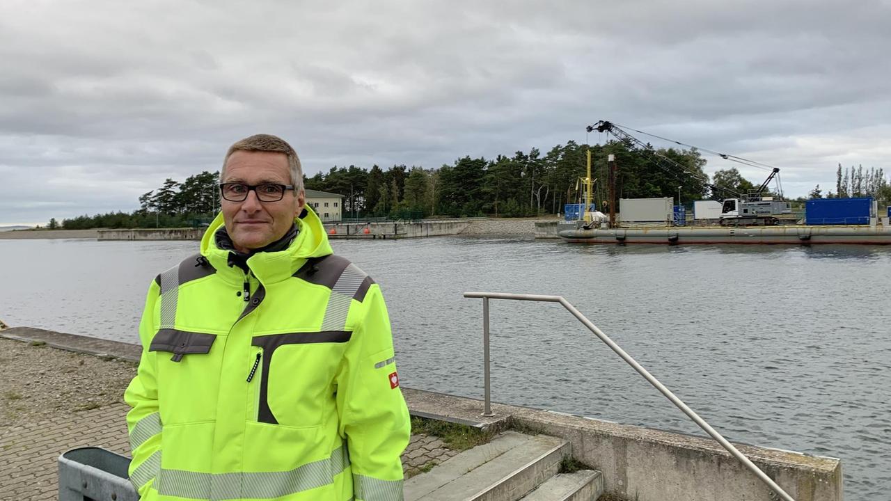 Lubminer Bürgermeister Axel Vogt steht in einer gelben Warschutzjacke am Ufer.