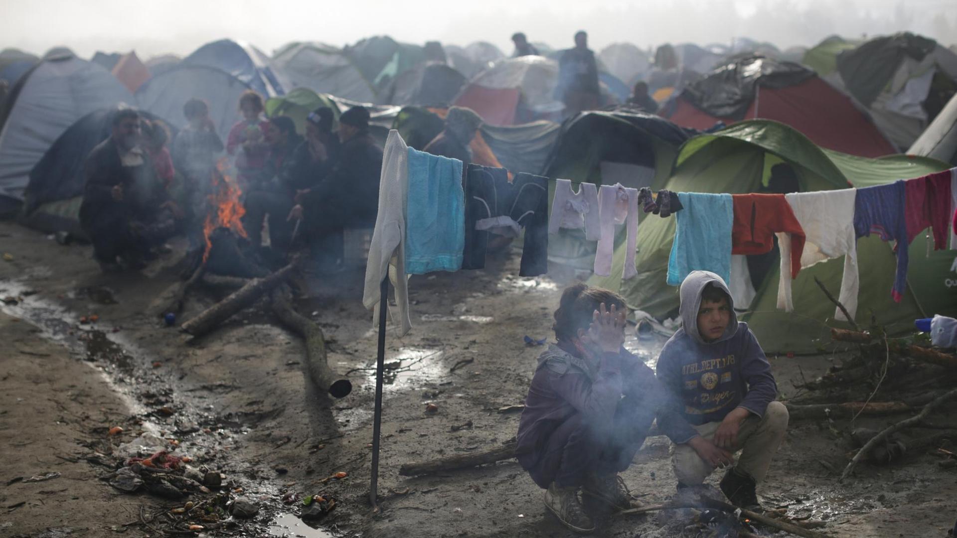 Zwei Flüchtlingskinder sitzen im Flüchtlingslager in Idomeni an der Grenze zwischen Griechenland und Mazedonien an einer Feuerstelle. Starker Regen und Temperaturen um die fünf Grad haben die Situation der Flüchtlinge noch erschwert.