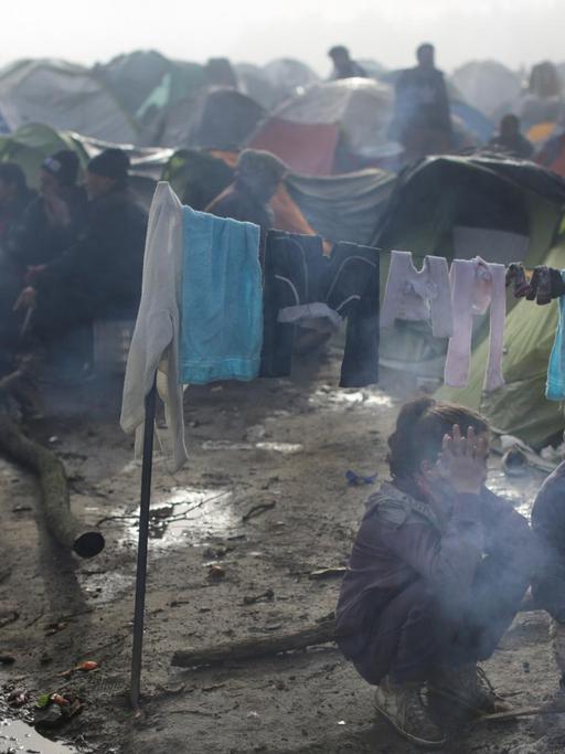 Zwei Flüchtlingskinder sitzen im Flüchtlingslager in Idomeni an der Grenze zwischen Griechenland und Mazedonien an einer Feuerstelle. Starker Regen und Temperaturen um die fünf Grad haben die Situation der Flüchtlinge noch erschwert.