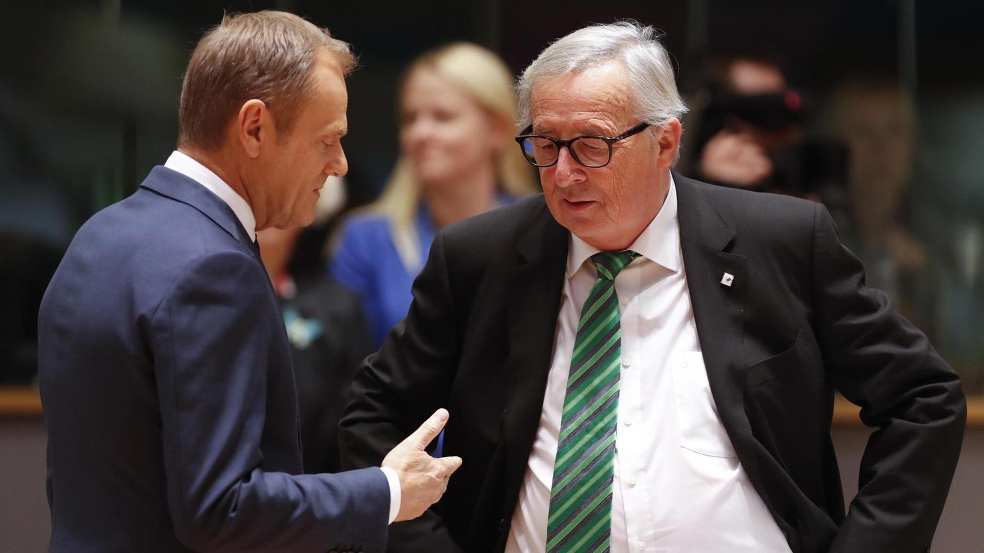 Donald Tusk (l) und Jean-Claude Juncker unterhaltenm sich. Tusk gestikuliert dabei mit der rechten Hand.