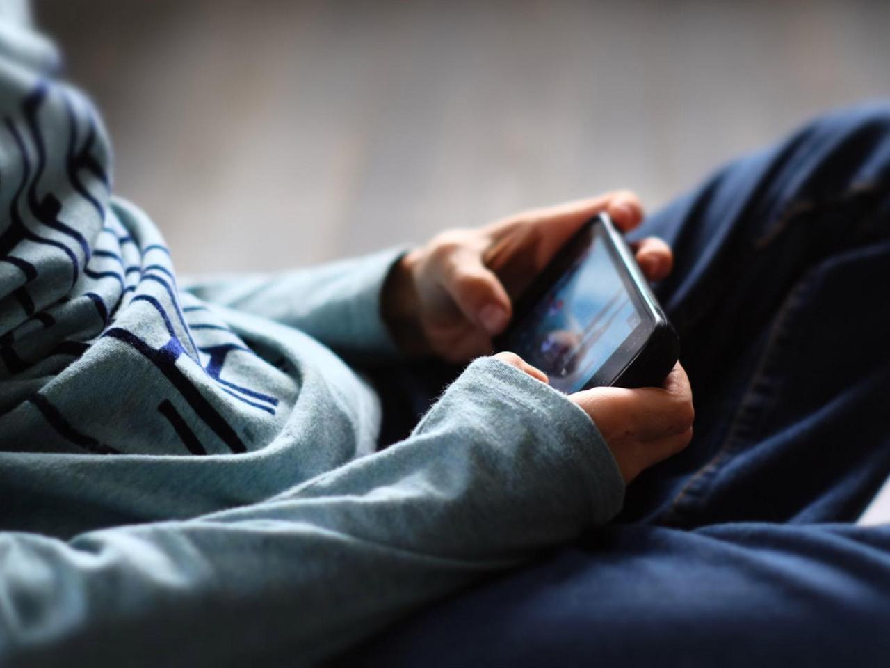 Oberjörper eines Jungen, der sitzend mit dem Handy spielt (Symbolbild)
