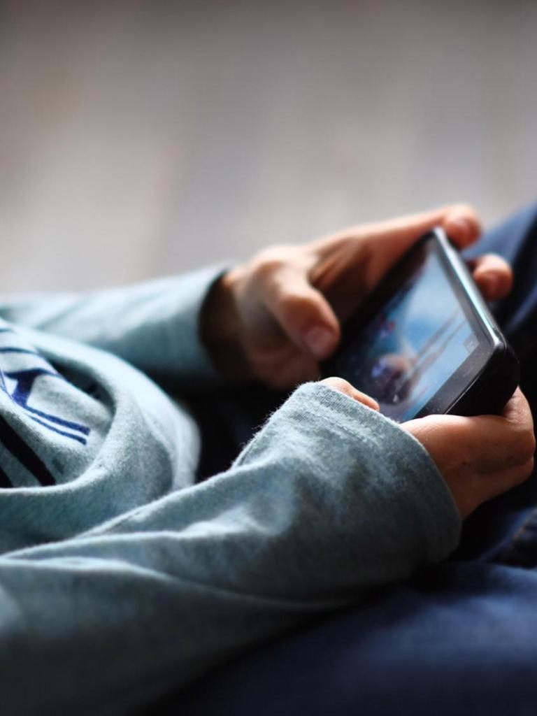 Oberjörper eines Jungen, der sitzend mit dem Handy spielt (Symbolbild)