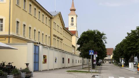 Ein klassizistischer Gefängnisbau, gelb angestrichen, liegt direkt an einer Straße mit Bäumen gesäumt.
