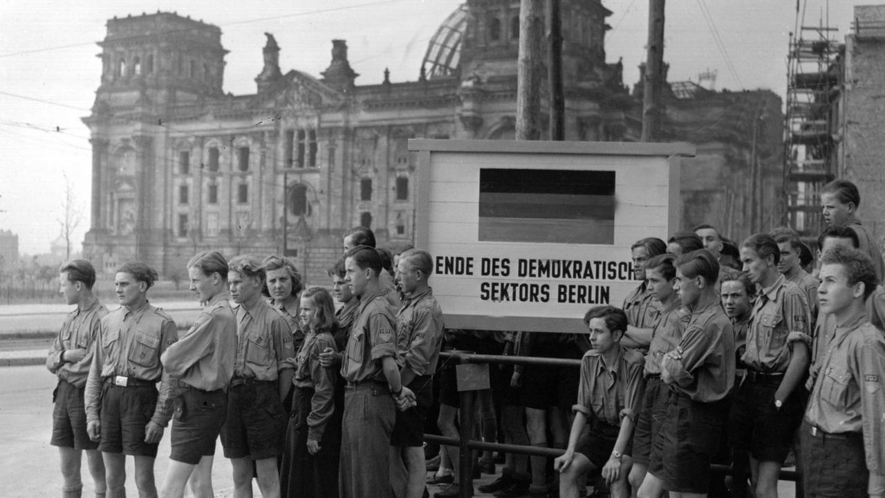 FDJ-Angehörige blicken vom Brandenburger Tor aus in den westlichen Teil Berlins. Angehörige der Volkspolizei warnten die Jugendlichen, daß sie bei Betreten West-Berlins von der dortigen Polizei verhaftet werden würden (undatiert). Die "Freie Deutsche Jugend" (FDJ), der einheitliche Jugendverband der sowjetischen Besatzungszone, wurde am 7. März 1946 im sowjetischen Sektor zugelassen und beging am 8. November 1947 in Berlin seine Gründungsfeier. Nach der Gründung der DDR 1949 war die FDJ der einzige zugelassene Verband für Jugendliche ab 14 Jahren. Zu den Aufgaben des FDJ gehörten die politische und ideologische Erziehung der Jugend. Außerdem betreute er den Kinderverband der DDR, die Pionierorganisation "Ernst Thälmann", die sogenannten Jungen Pioniere.