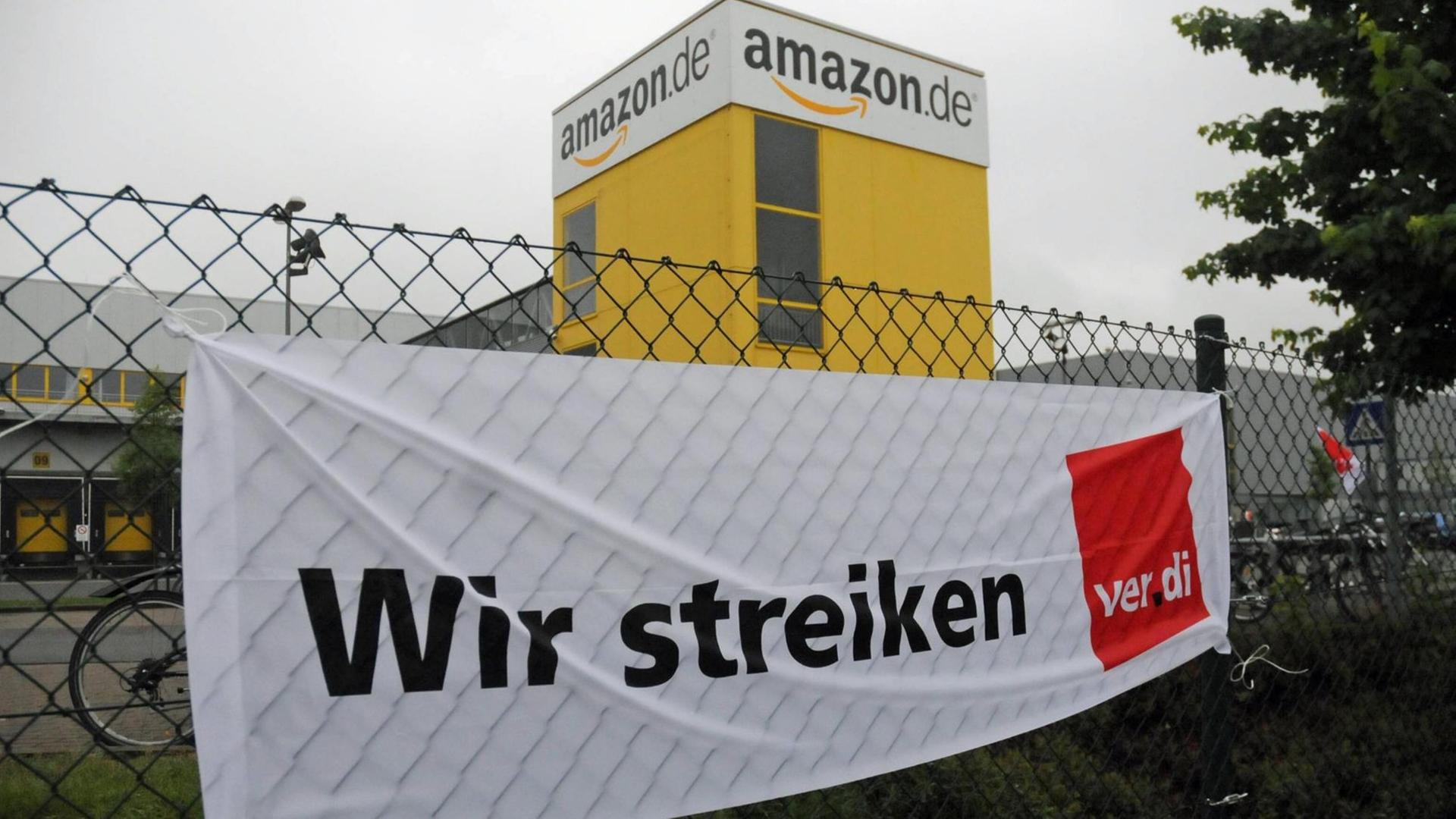 Am Zaun vor dem Amazon-Lager in Leipzighängt ein Verdi-Plakat mit der Aufschrift "Wir streiken"