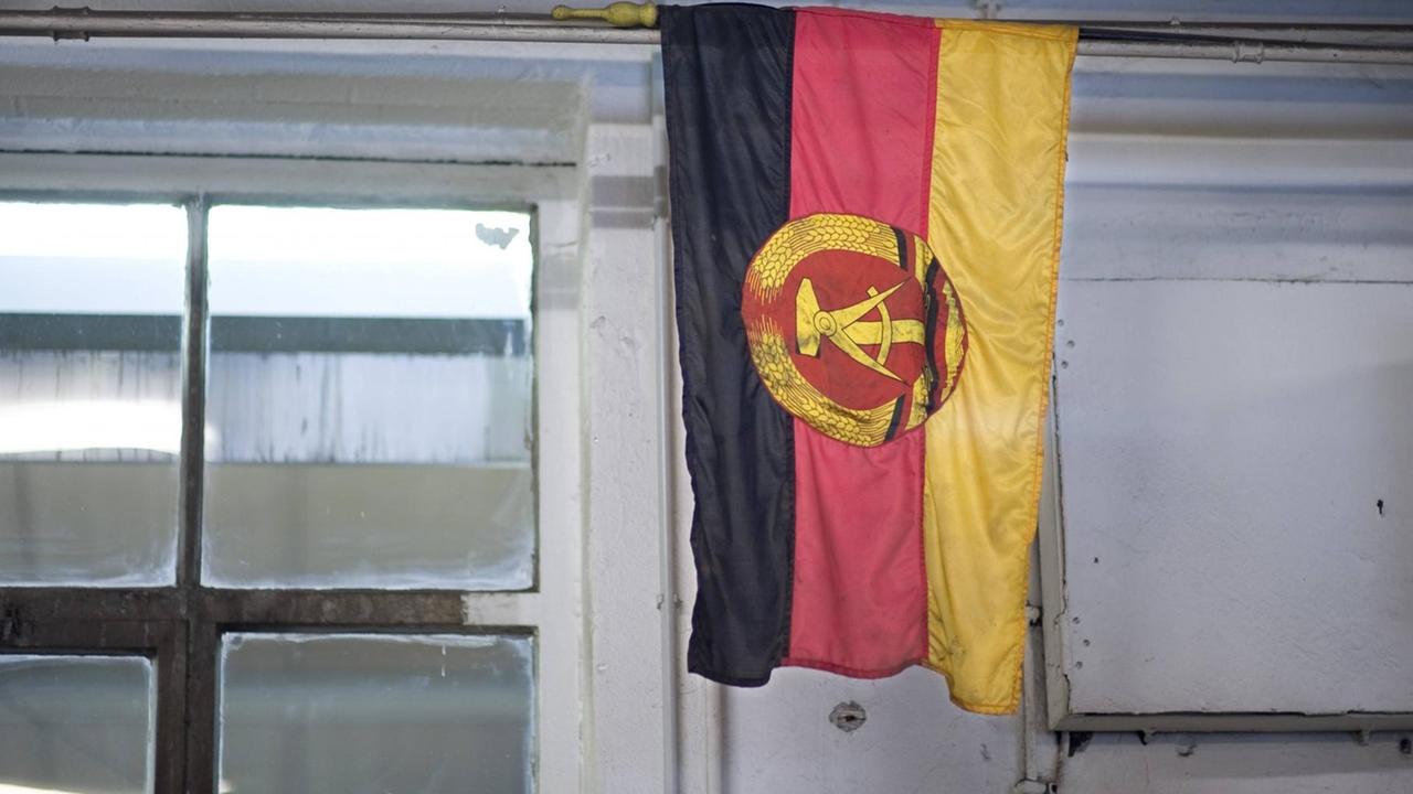 Eine Flagge der ehemaligen DDR hängt in einem Raum mit Fenster.