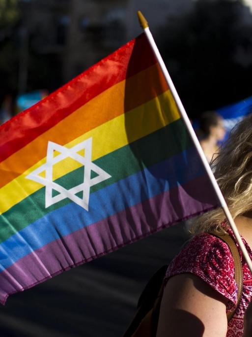 Eine Frau hält während einer Gay-Pride-Parade in Jerusalem 2016 eine Regenbogenfahne mit einem Davidstern in der Mitte in der Hand.