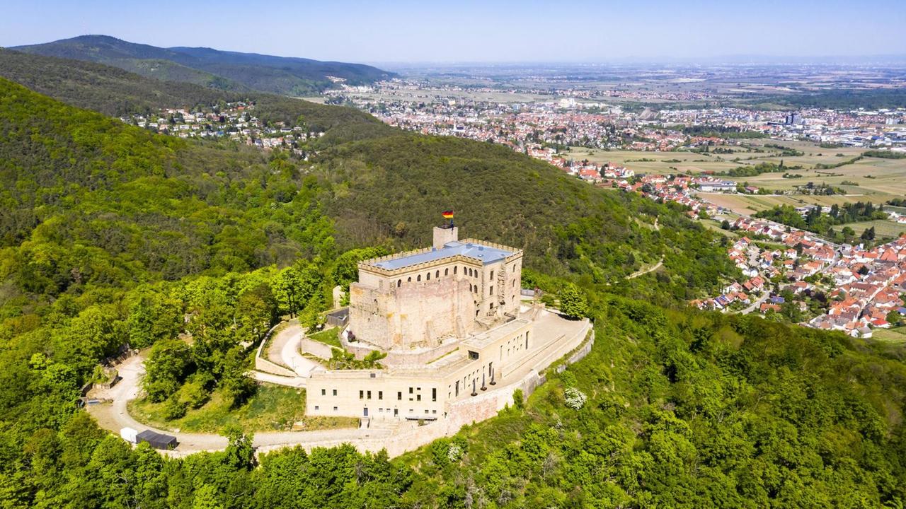 Helikopterblick auf die teilerhaltene Burg- bzw. Schlossanlage auf einem bewaldeten Berg mit Blick auf die nahe Gemeinde.