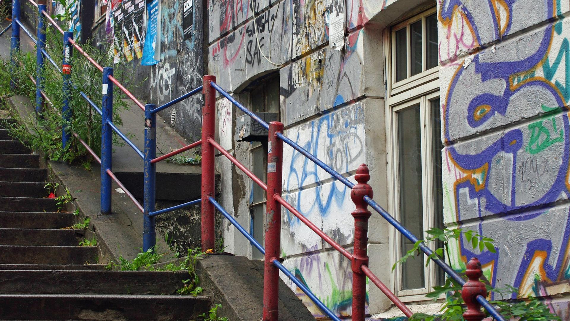 Ein Haus mit Graffitis an einer Treppe mit buntem Geländer