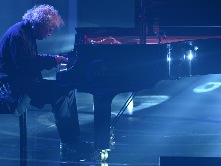 Der Pianist Joachim Kühn spielt auf einer blau erleuchtenden Bühne an einem Flügel.