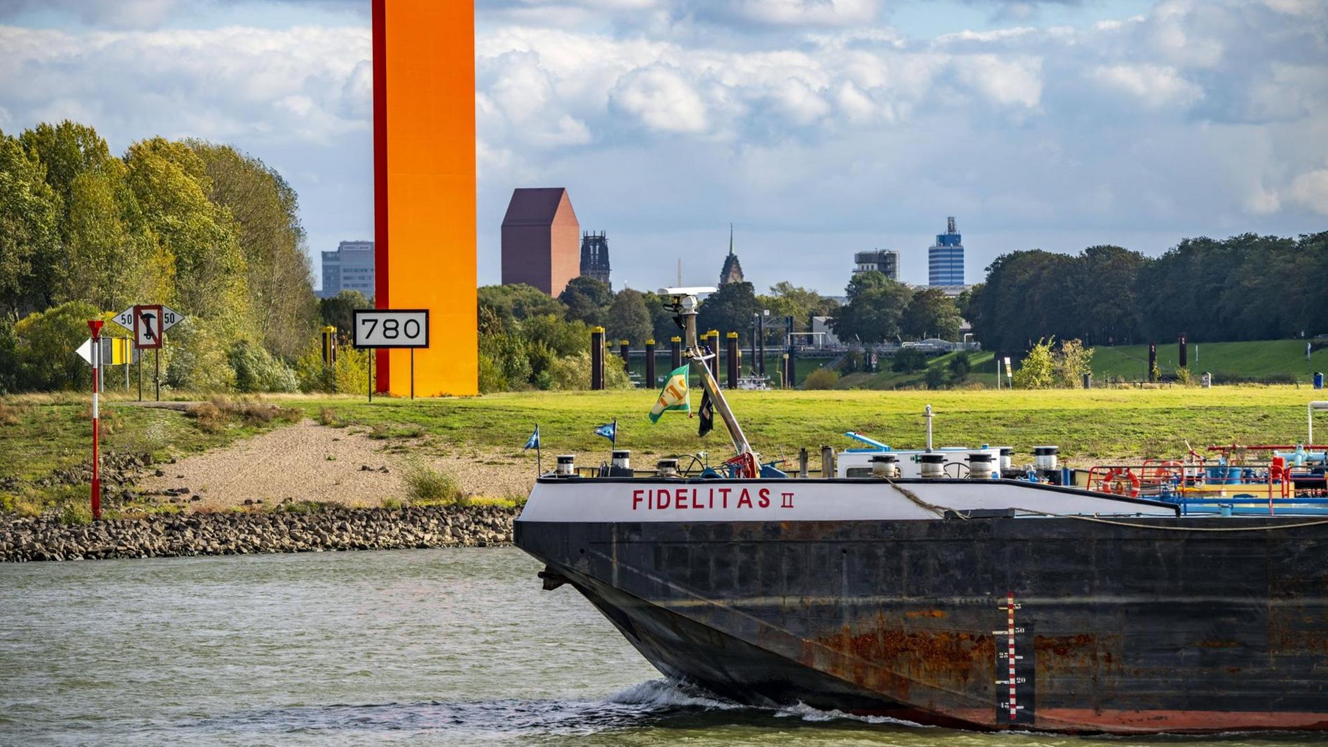 Die Skulptur Rheinorange an der Mündung der Ruhr in den Rhein. Im Hintergrund die Skyline der Innenstadt von Duisburg.