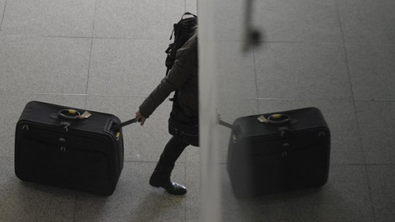 Ein Reisender verschwindet mit seinem Koffer hinter einer Ecke