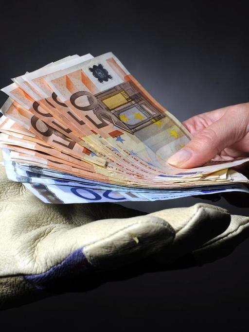 Eine Hand mit einem Arbeitshandschuh nimmt 560 Euro entgegen.