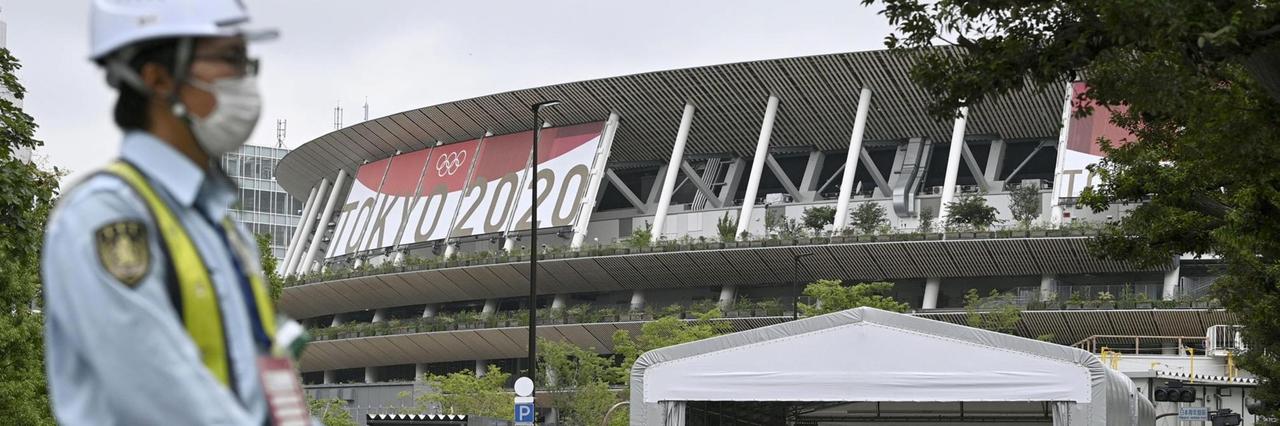 Ein Sicherheitsbeamter in Tokio trägt eine Schutzmaske und steht vor dem Nationalstadion.
