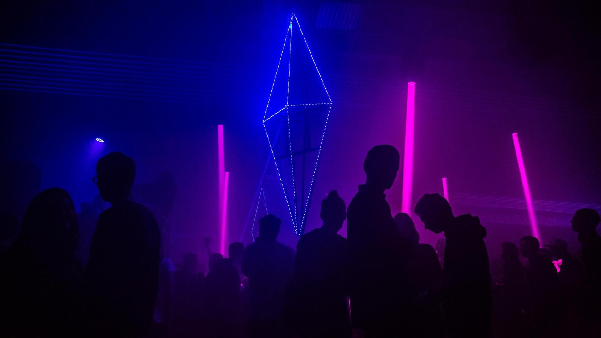 Silhouetten von tanzenden Menschen in einem Club, vor pinkten und blauen Neonröhren.