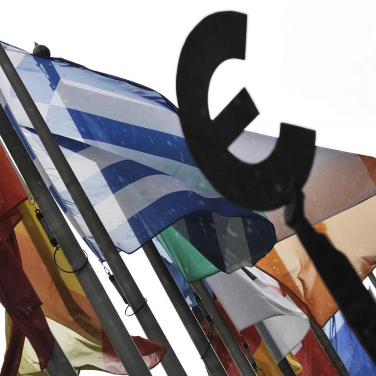 Flaggen vor dem EU-Parlament in Brüssel, davor eine Frauen-Statue, die das Eurozeichen in der Hand hält