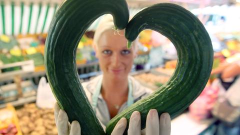 Eine Gemüsehändlerin zeigt am 30.06.2009 auf dem Isemarkt in Hamburg zwei krumme Gurken in Herzform.