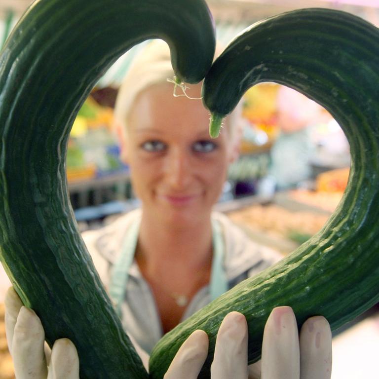 Eine Gemüsehändlerin zeigt am 30.06.2009 auf dem Isemarkt in Hamburg zwei krumme Gurken in Herzform