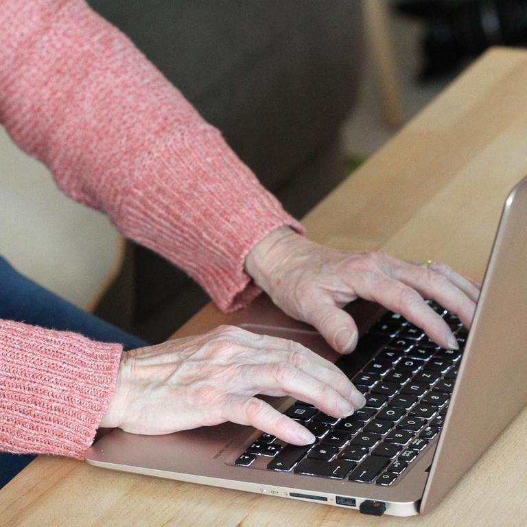 Hände einer Seniorin auf der Tastatur eines Laptops.