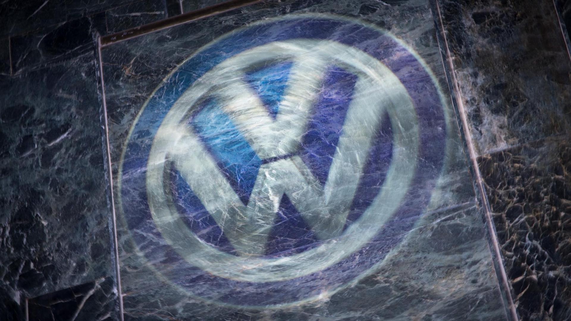 Das Logo von VW mit einer zerkratzten Glasplatte darüber.