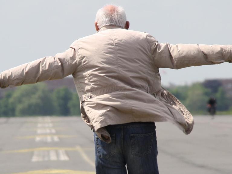 Ein älterer Mann läuft über das Tempelhofer Feld und breitet die Arme aus.