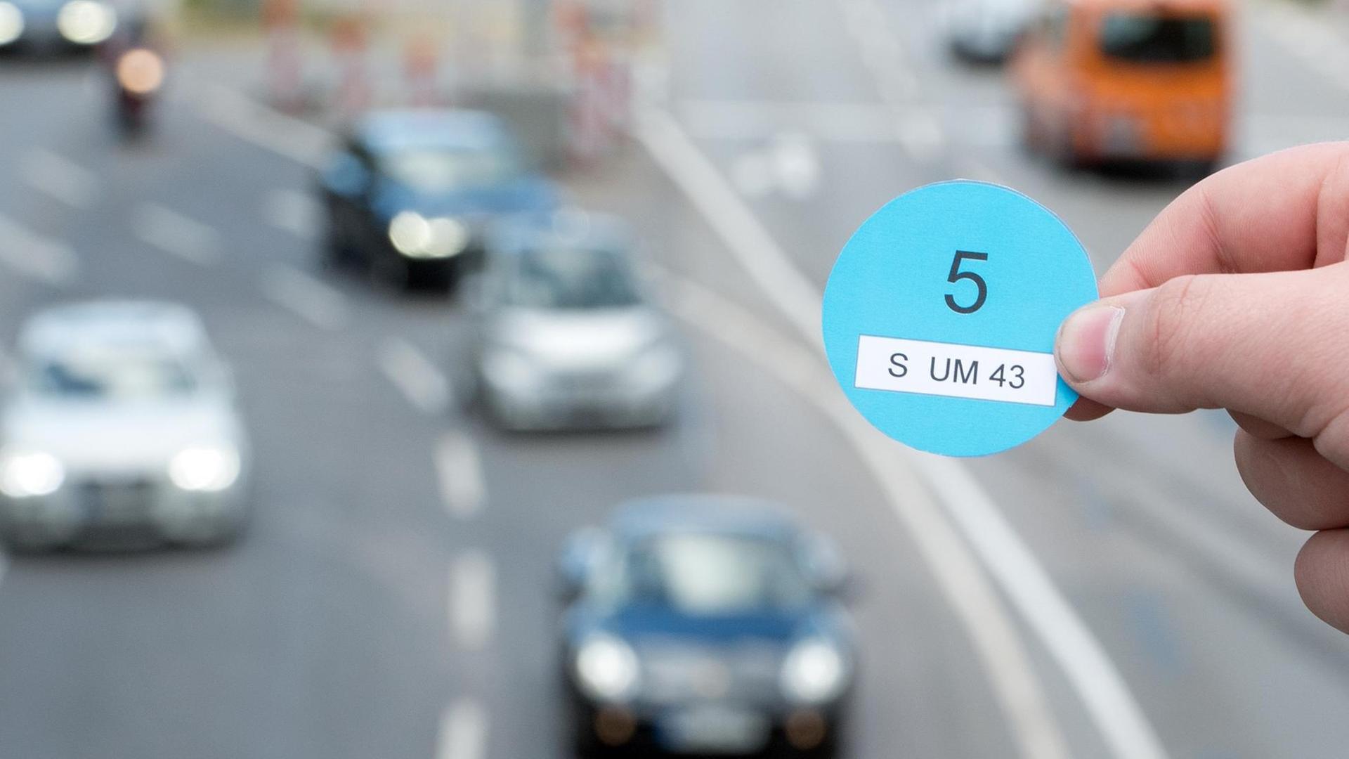 Eine Hand hält am 05.10.2016 einen Designvorschlag des Verkehrsministeriums Baden-Württemberg in der Innenstadt von Stuttgart (Baden-Württemberg) vor vorbeifahrenden Autos (gestellte Szene).