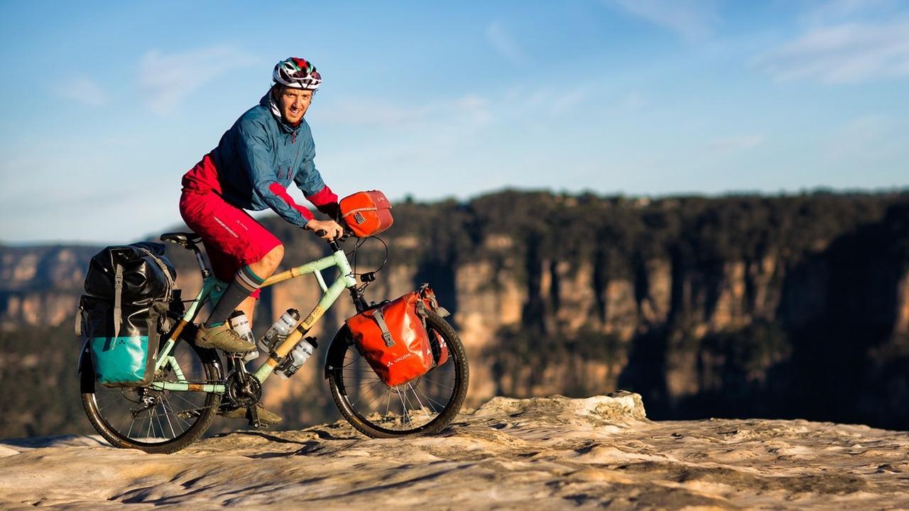 Bamboo Basti fährt auf seinem Fahrrad aus Bambus an einem felsigen Abgrund in Australien entlang.