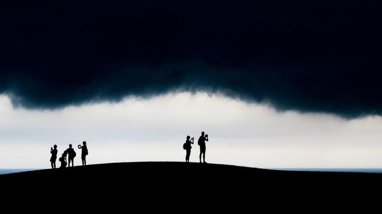 Menschen stehen auf einer Anhöhe und machen Bilder von einer tief hängenden schwarzen Wolke