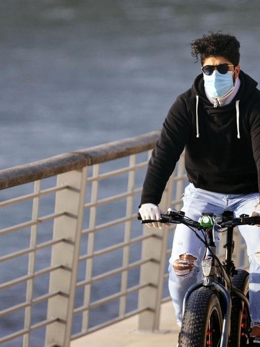 Ein Radfahrer mit Atemschutzmaske zum Schutz vor dem Coronavirus am Rheinboulevard in Köln.