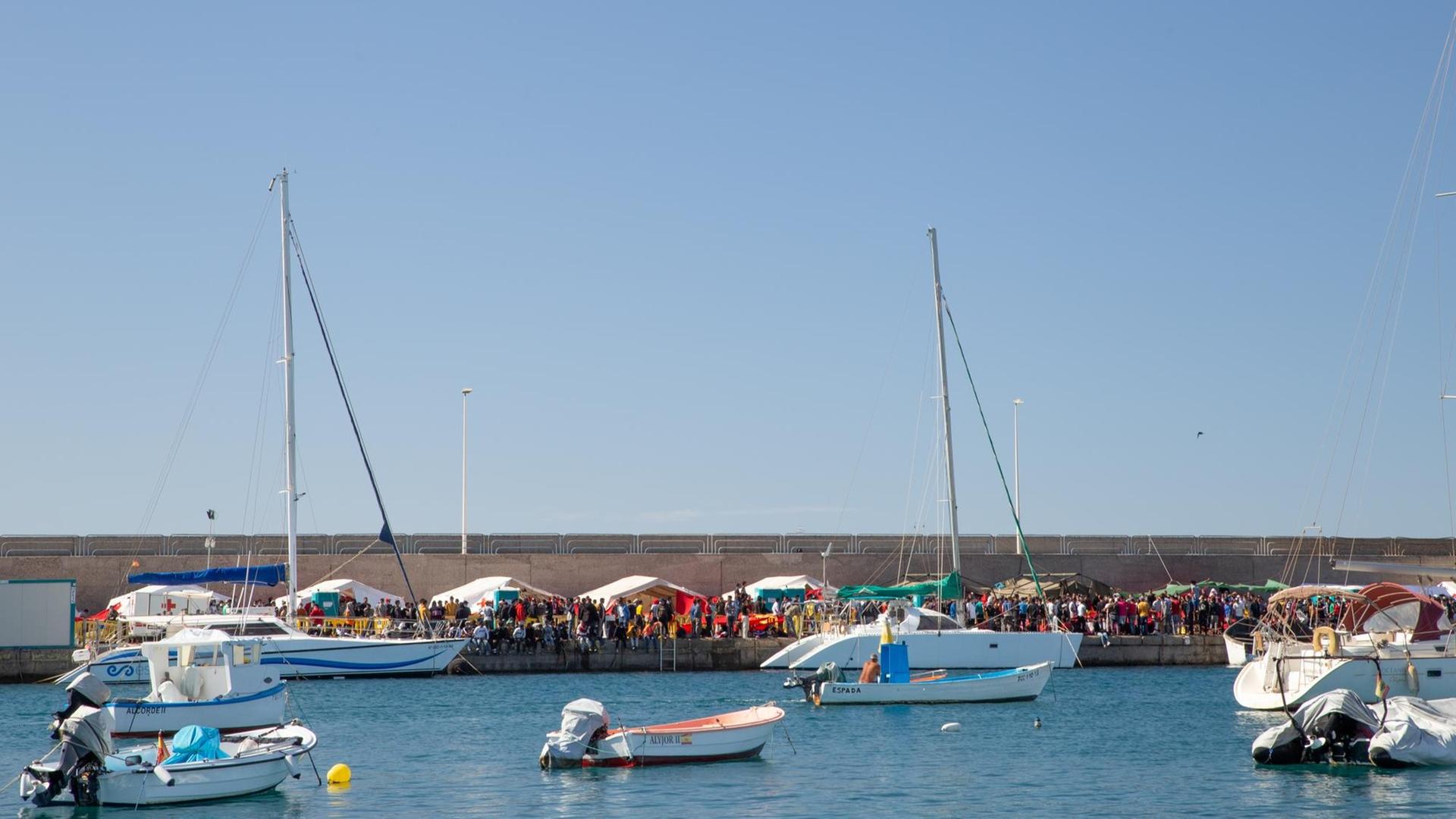 Blick auf den Hafen von Arguineguín. Im Hafenbecken Boote, an Land Zelte, an denen sich Menschen drängen.