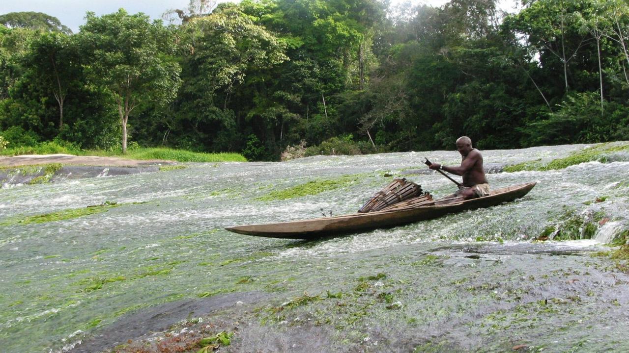 Mann aus Kajan in einem Einbaum manoevriert in einer Stromschnelle des Marowijne Flusses, Surinam