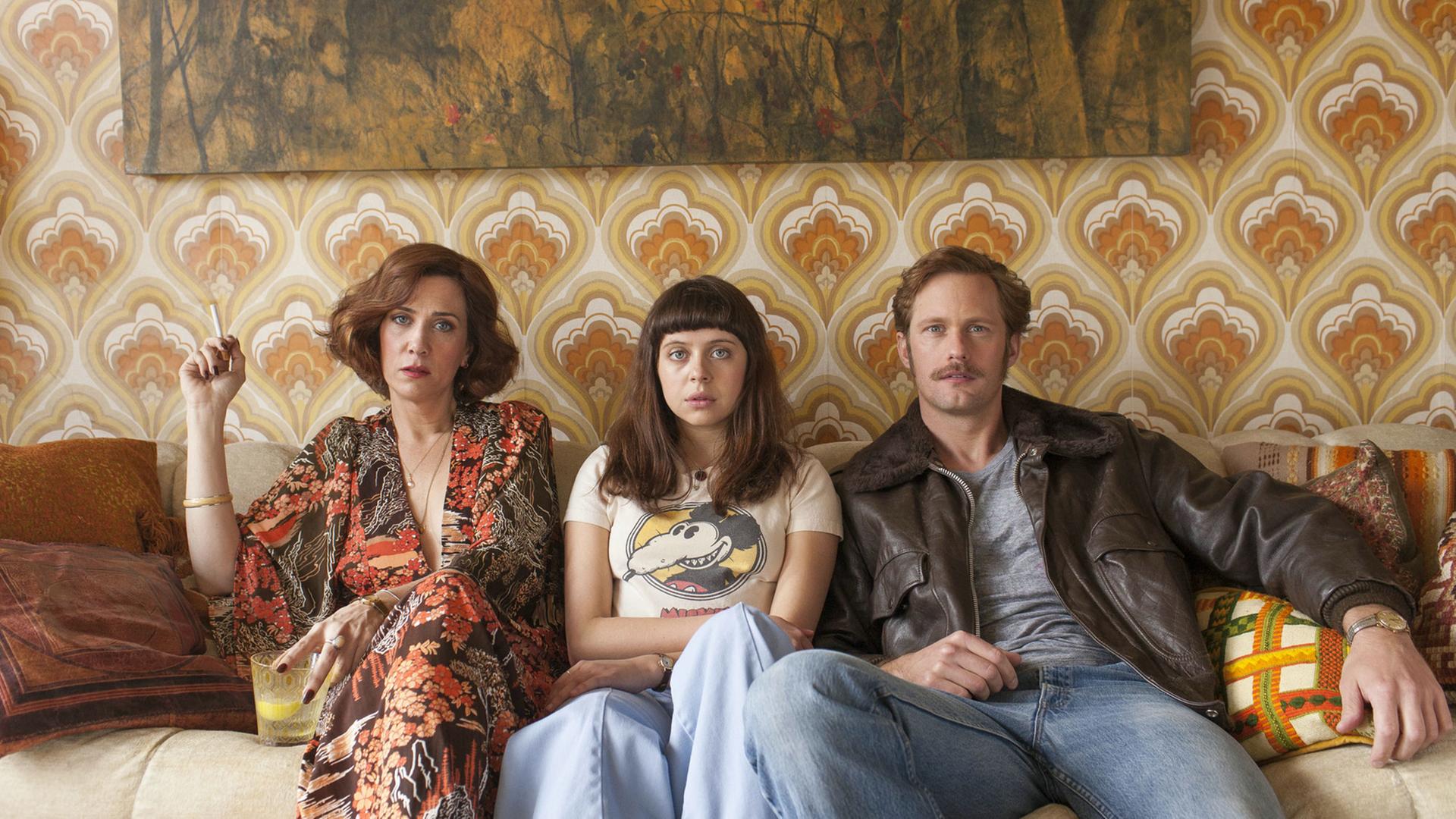 Kristen Wiig als Charlotte Goetze, Bel Powley als Minnie Goetze und Alexander Skarsgard als Monroe sitzen in einer Szene des Films "The Diary of a Teenage Girl" nebeneinander auf einem Sofa.