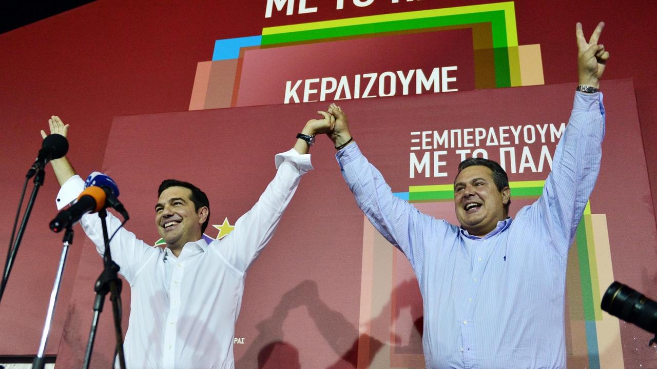 Die griechischen Politiker Alexis Tsipras (Syriza) und Panos Kammenos (Anel) stehen nebeneinander auf einer Bühne und reißen die Arme in die Höhe.