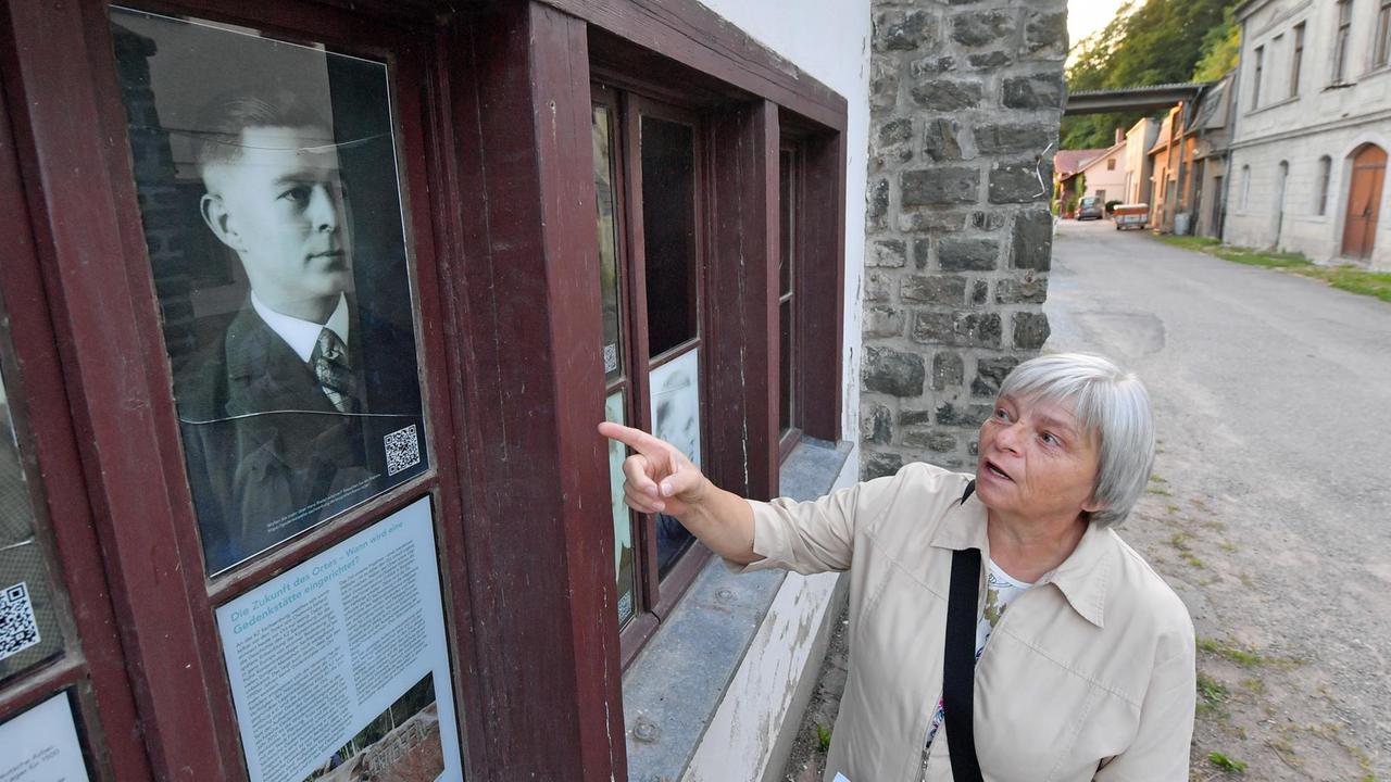 Neben einem Porträtfoto ihres Großvaters Hans Riedel steht Gisela Heiden am Eingang zum ehemaligen KZ Sachsenburg in Frankenberg (Sachsen).