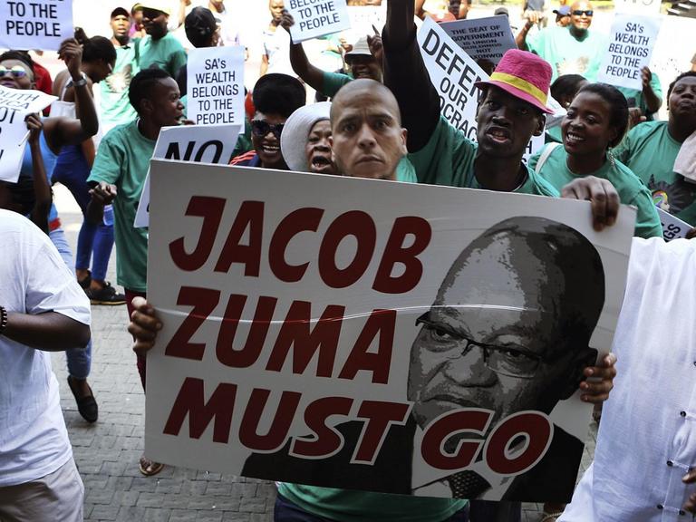 Demonstranten protestieren gegen den südafrikanischen Präsidenten Jacob Zuma; auf einem Transparent steht "Zuma must go".