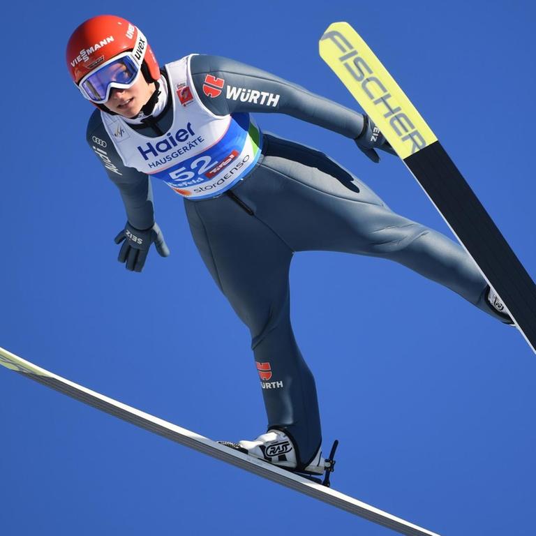 Das Bild zeigt Skispringen Katharina Althaus in der Luft vor einem blauen Himmel.