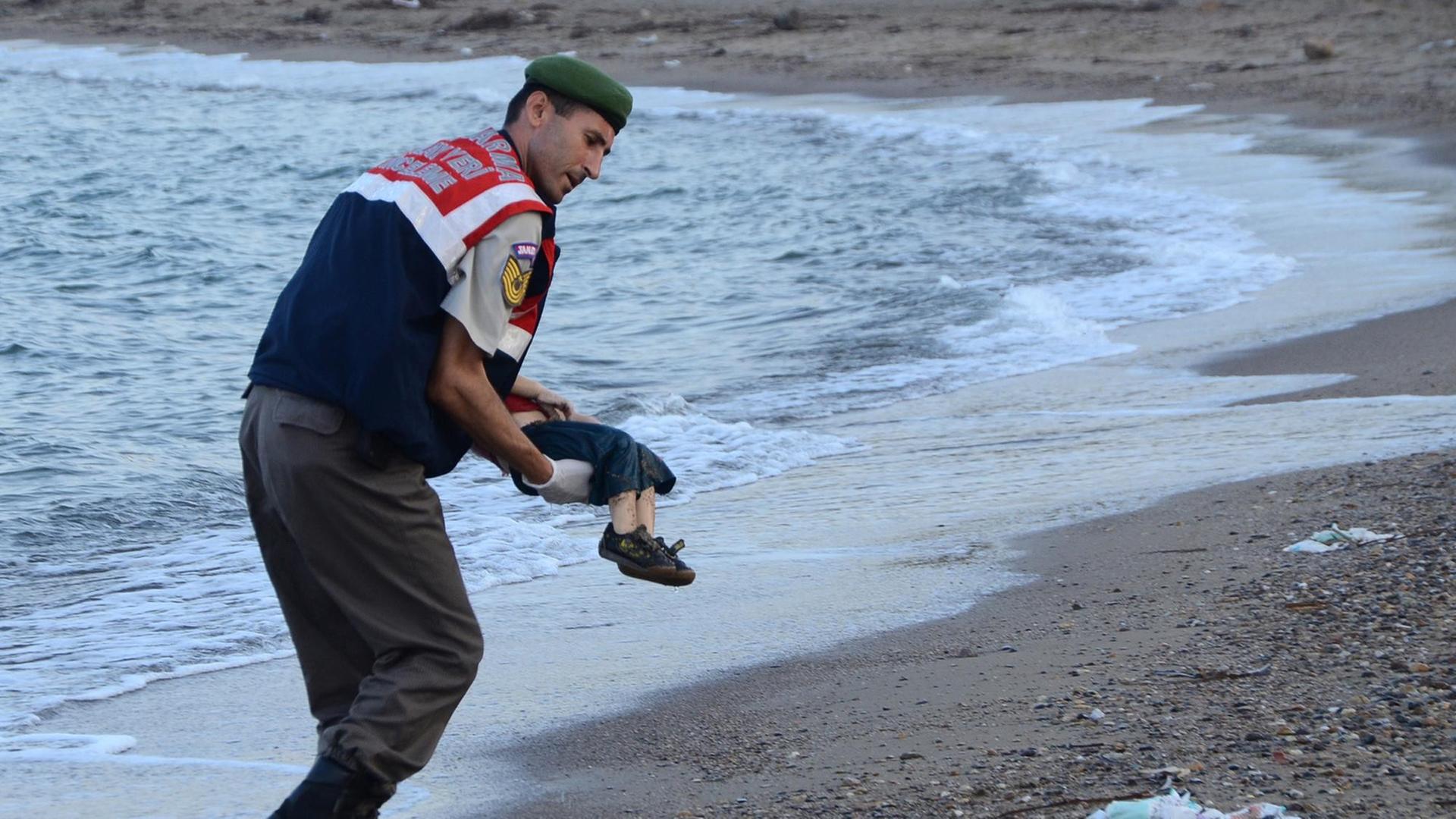Ein türkischer Polizist trägt ein totes Kind im Arm und bringt es vom Strand weg. Der Oberkörper des Kindes wird vom Körper des Polizisten verdeckt..