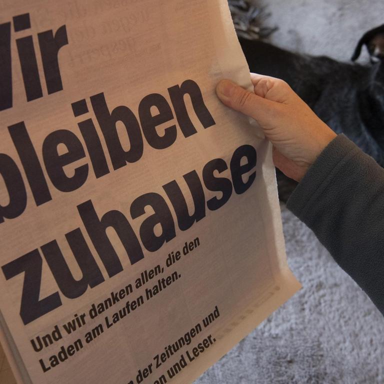 ILLUSTRATION: Eine Frau sitzt Zuhause neben ihrem Hund und schaut auf die Anzeige der Zeitungen unter dem Leitmotiv "Wir bleiben zuhause".